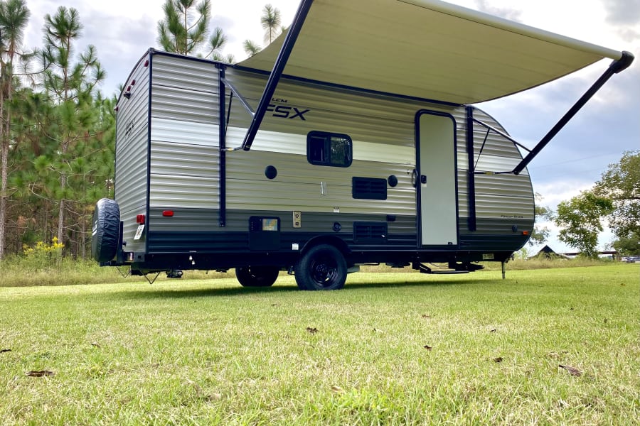 Our RV rental: a modern travel trailer with awning extended, parked on green grass, ready for your outdoor adventure.