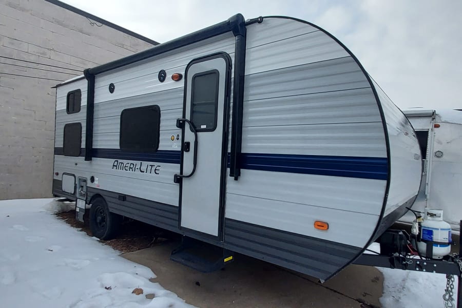 Ameri-Lite travel trailer, great for RV rental, parked on a snowy lot against a brick wall.