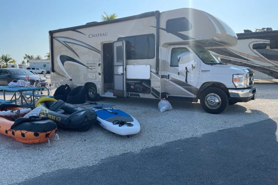 Sunny day with an RV rental parked on gravel. Inflatable boats & paddleboard are outside, ready for outdoor fun.