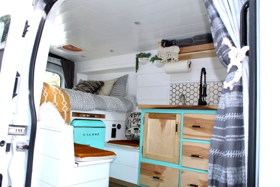 Experience cozy RV rental living! This camper van features a comfy bed, compact kitchen with a Galanz fridge, and stylish decor.