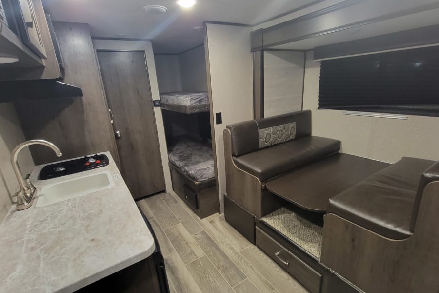 Explore this RV rental interior, featuring a practical kitchenette, cozy bunk beds, and a comfortable dinette.