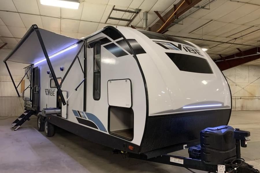 A white Vibe travel trailer RV, ready for rv rental adventures, featuring an extended awning and steps.