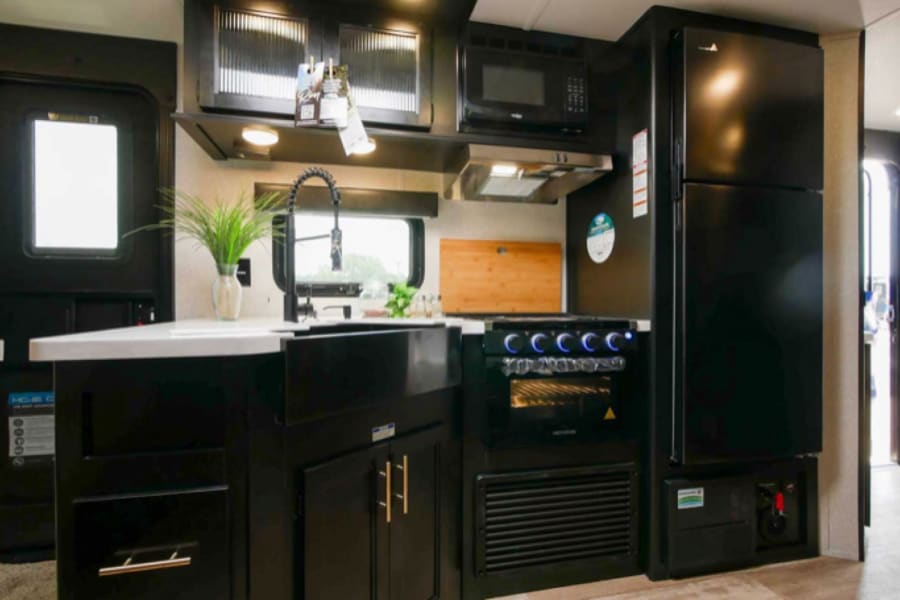 RV rental: modern kitchen with black cabinets, sink, microwave, stove, and fridge.