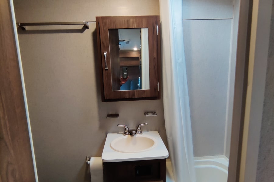 Compact RV rental bathroom with sink, toilet, shower/tub combo, and overhead skylight.