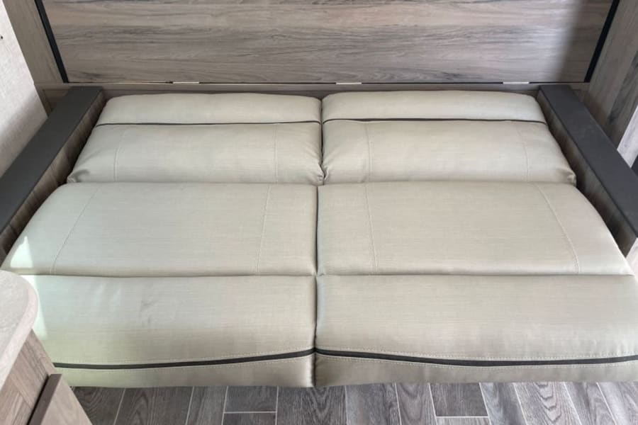 RV rental interior: A beige convertible sofa bed with dark trim and wood paneling, ready for relaxation or sleep.