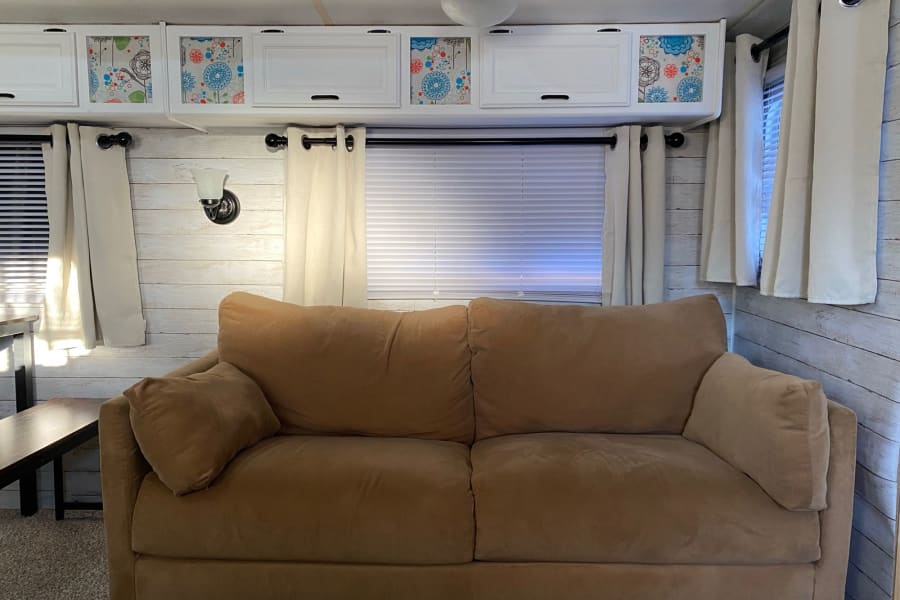 Inside a stylish **rv rental** featuring a tan sofa, shiplap walls, and unique floral cabinet inserts.