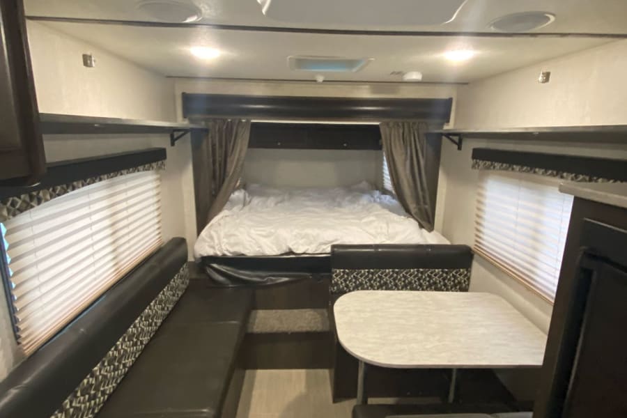 View of an RV rental's interior, showing a bed, dinette, windows, and overhead storage, designed for comfortable travel.