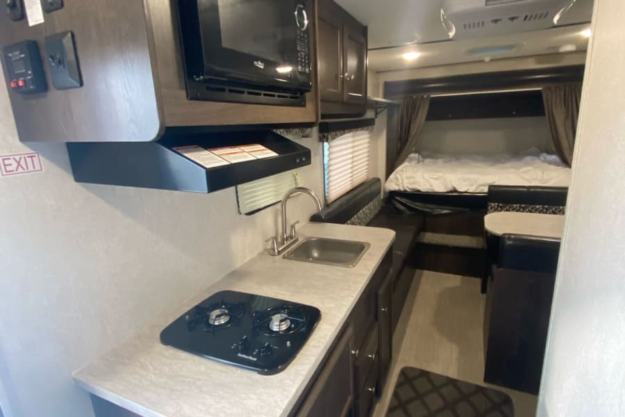 Inside this RV rental: a compact kitchen with microwave & stove, dining area, and cozy bedroom. Perfect for travel.