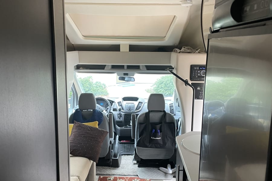 RV rental interior: view to front cabin with driver's area, comfy seating, kitchen appliance & patterned rug. Ready for travel!