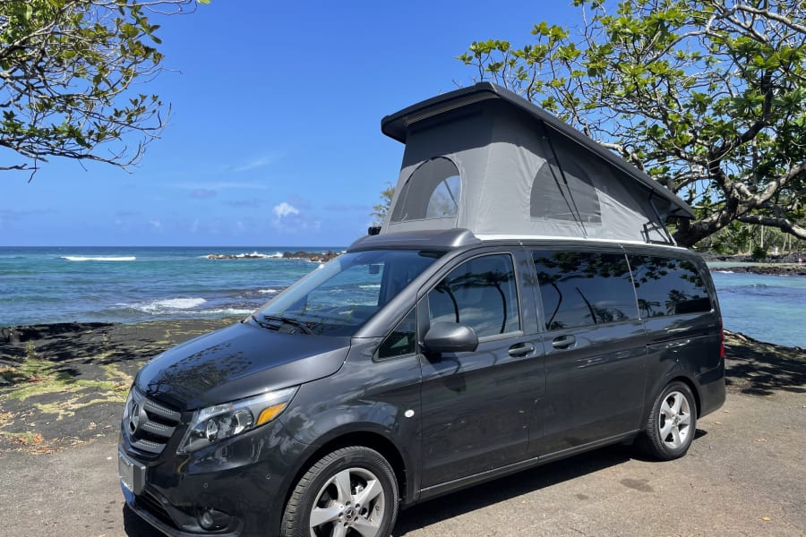 Dark grey pop-top camper van rv rental by Hawaii's coast. Enjoy scenic ocean views & nature adventures.