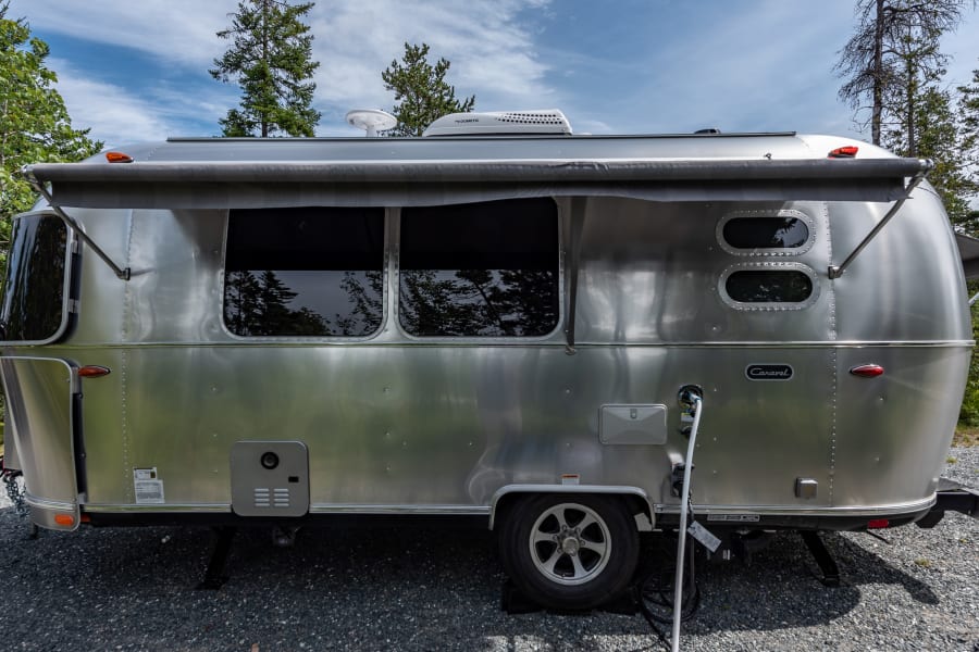 This gleaming silver Airstream travel trailer, great for an RV rental, is parked outdoors on gravel with its awning extended.