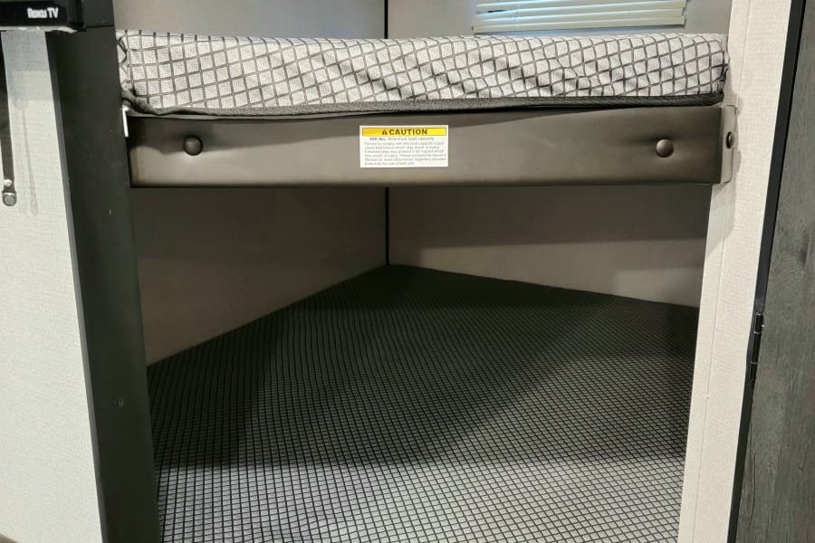 An RV rental bunk bed with safety netting and window. A caution label for elevated beds and a Roku TV are visible.