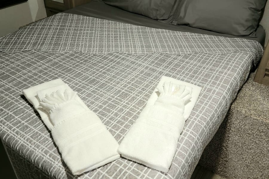Cozy RV rental bedroom featuring neatly folded fresh towels on patterned bedding, a nightstand, and wood-look flooring.