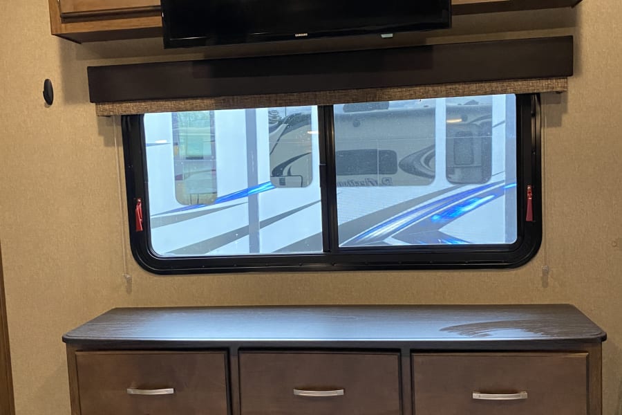 RV rental interior featuring a wall-mounted TV, window, and wood-toned dresser with silver pulls.