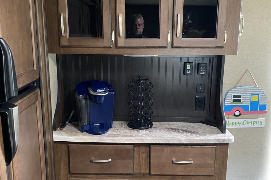 RV rental kitchen area with Keurig, wood cabinets, and a man's reflection clearly visible in the glass.