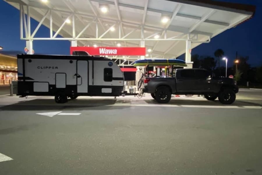 This RV rental and truck, packed with a paddleboard and bike, refuels at a Wawa gas station at night.