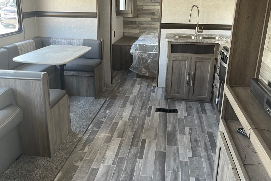 Modern RV rental interior with sleek kitchen, dining booth, and wood-look plank flooring.