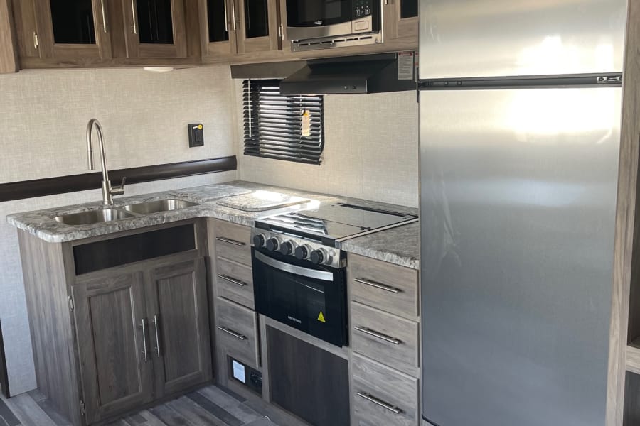 RV rental kitchen: stainless steel fridge, microwave, range, sink, and wood-grain cabinets on a gray plank floor.