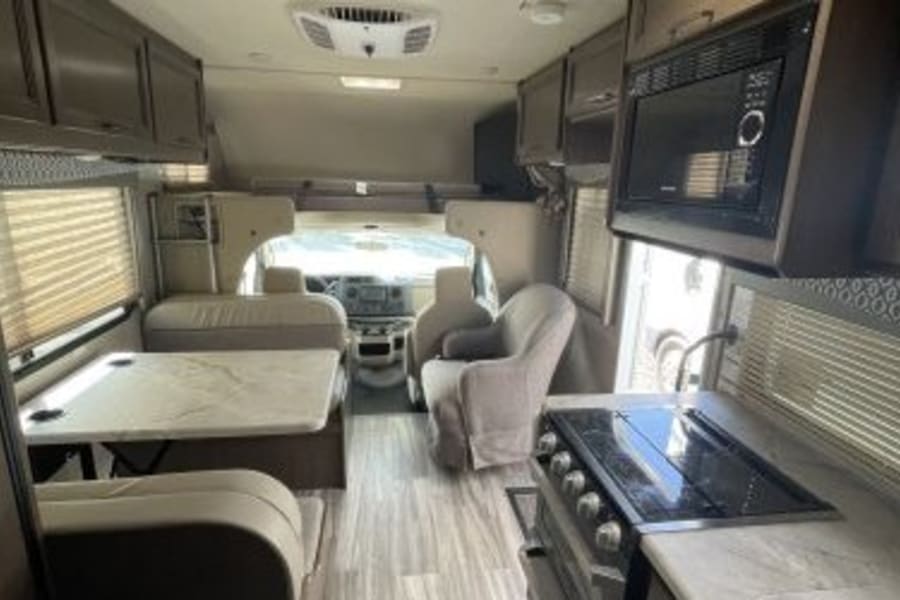 This spacious RV rental interior features a modern kitchen, dining table, and living space, looking towards the cockpit.