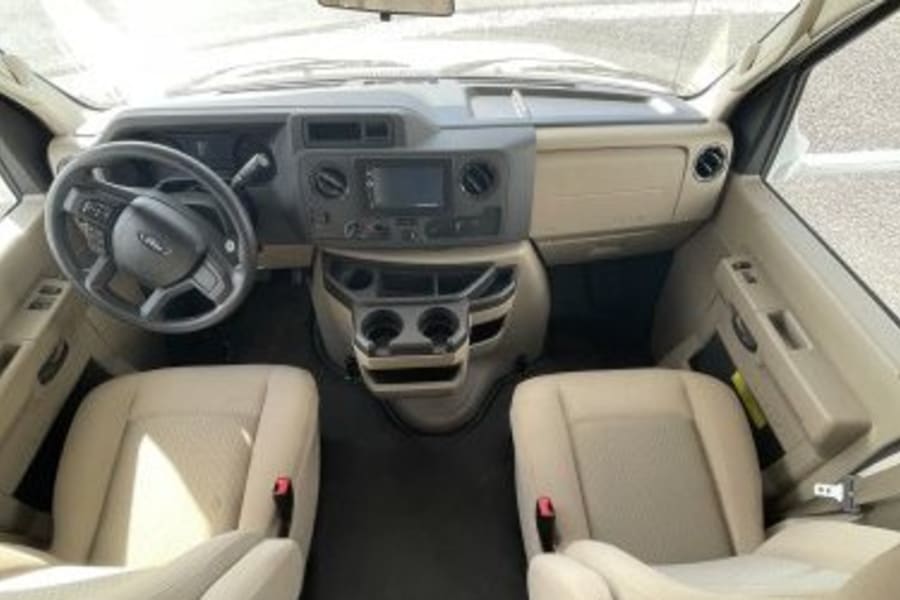 This RV rental's spacious tan interior shows the dashboard, steering wheel, central console with screen/cup holders, and front seats.