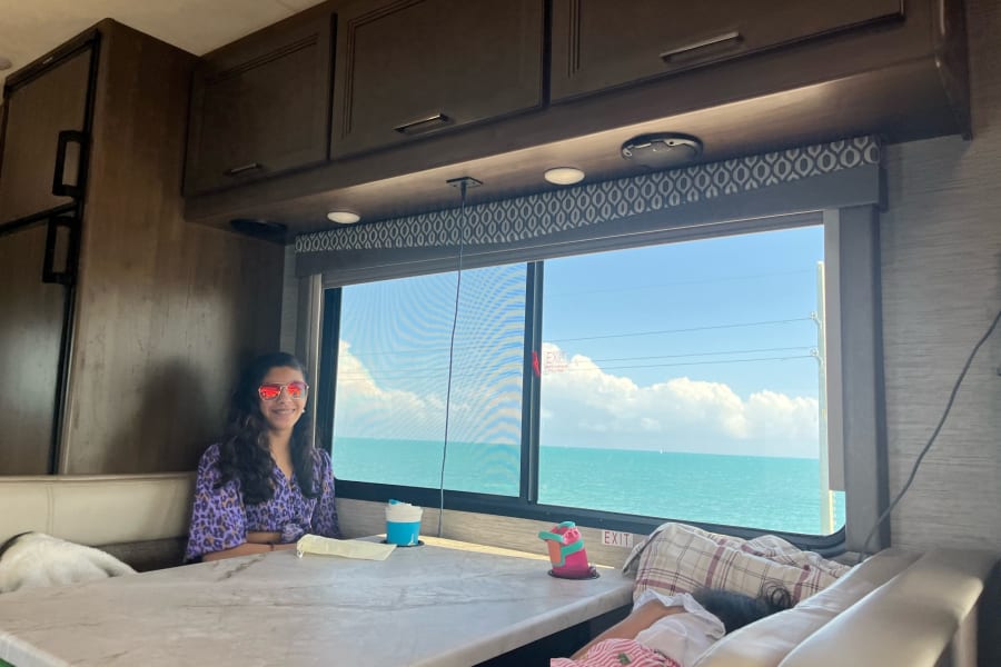 A girl in sunglasses and family relax in their RV rental, enjoying the stunning ocean view from inside.
