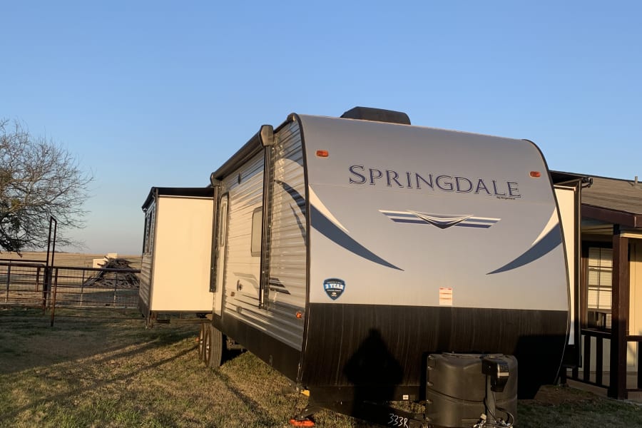 A Springdale travel trailer with a slide-out extended, an ideal rv rental, is parked on dry grass under a clear sky.