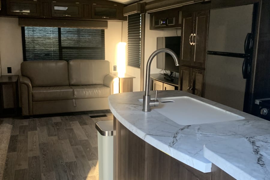 Inside this RV rental: a bright living area with a comfortable sofa and a modern kitchen island, ready for your travels.