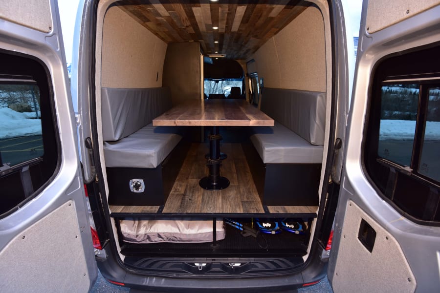 Inside an RV rental: a stylish camper van conversion with a wooden table, cozy benches, and ample rear storage.
