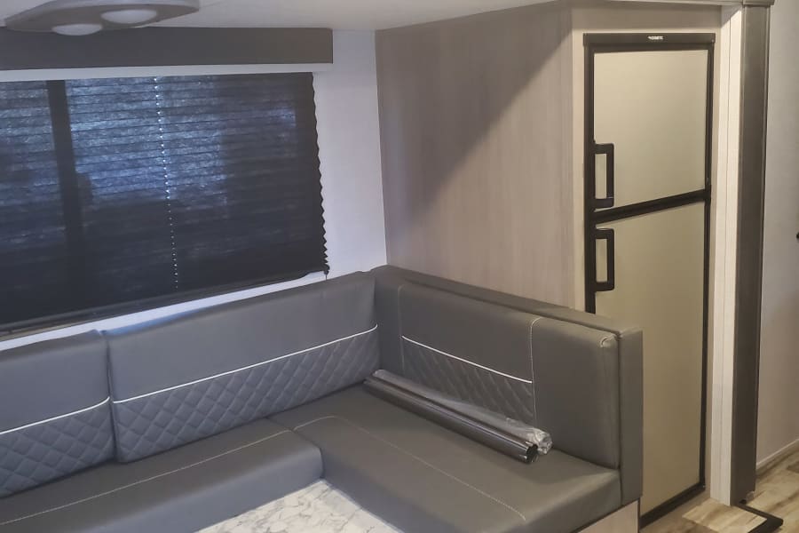 RV rental: Modern gray U-shaped dinette, marble table, overhead cabinets, and Dometic fridge in a spacious living area.