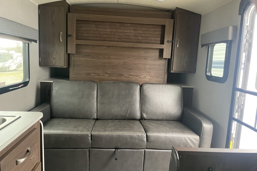 RV rental: Cozy interior featuring a sofa, fold-down bed, overhead storage, and windows.