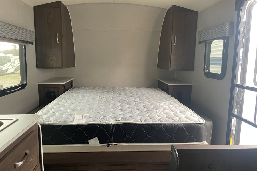 RV rental interior: compact bedroom with comfortable mattress, bedside storage, and overhead cabinets.