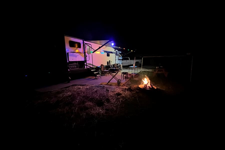 Cozy night at an RV rental campsite: colorful lights on the RV awning and a warm campfire glowing under the stars.