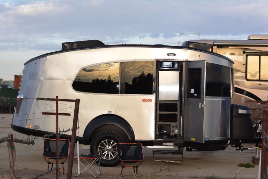 An Airstream Basecamp travel trailer, an excellent option for an RV rental, parked at a scenic campsite.