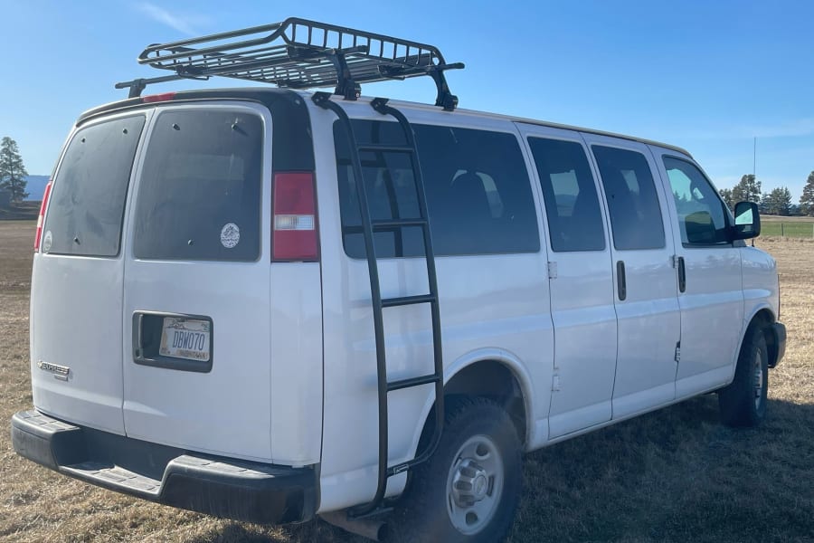 White camper van with a roof rack and rear ladder, parked on dry grass under a clear sky. Ideal for rv rental adventures.