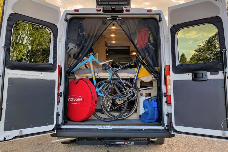 Rear view of an rv rental camper van with open doors, revealing two bicycles and gear for outdoor adventures.
