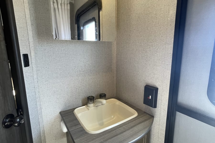 This RV rental offers a compact, functional washroom with a light-colored sink, mirror, and cabinet. Practical for travel.