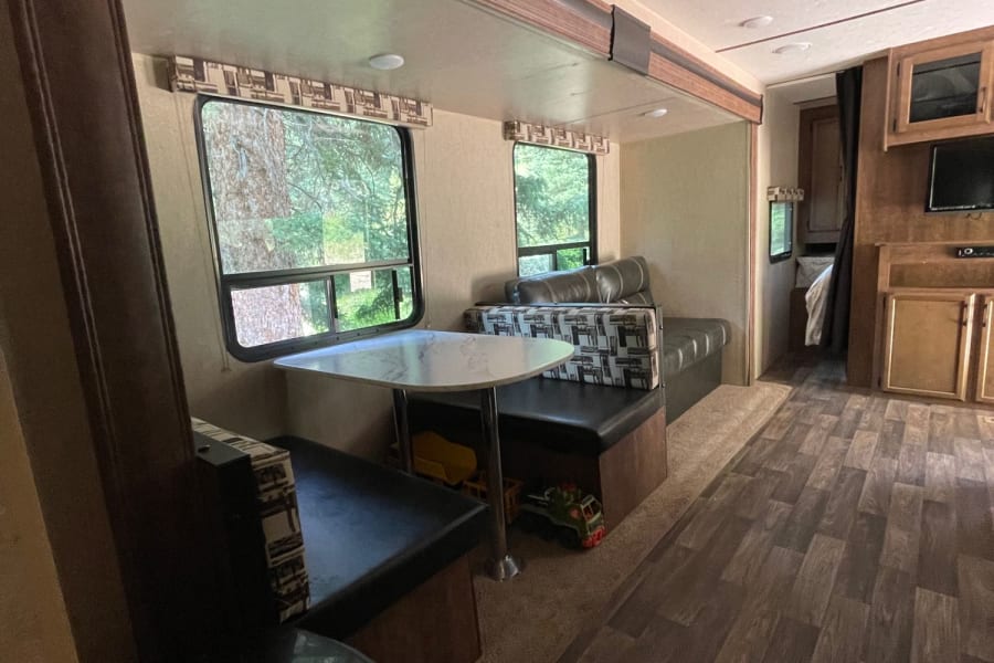 This RV rental's cozy interior features a dinette, comfy bench seating, wood floors, and windows with scenic views.