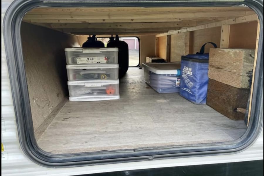Organized RV rental pass-through storage shows clear bins, utility hoses, leveling blocks, and propane tanks inside.