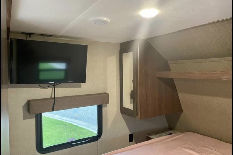 RV rental bedroom with wall-mounted TV, window, bed, and built-in storage. Perfect for road trips.