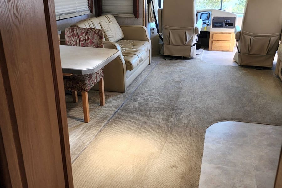 Spacious RV rental interior featuring a dining area, sofa, and cockpit seating on plush carpet.