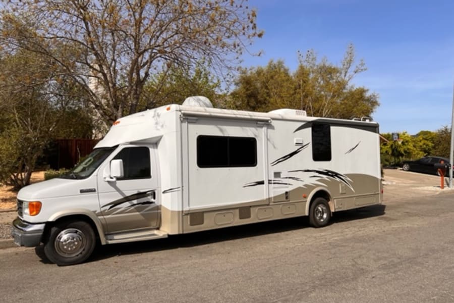 White & tan Class C RV rental parked outdoors. This spacious motorhome is ready for your next adventure.