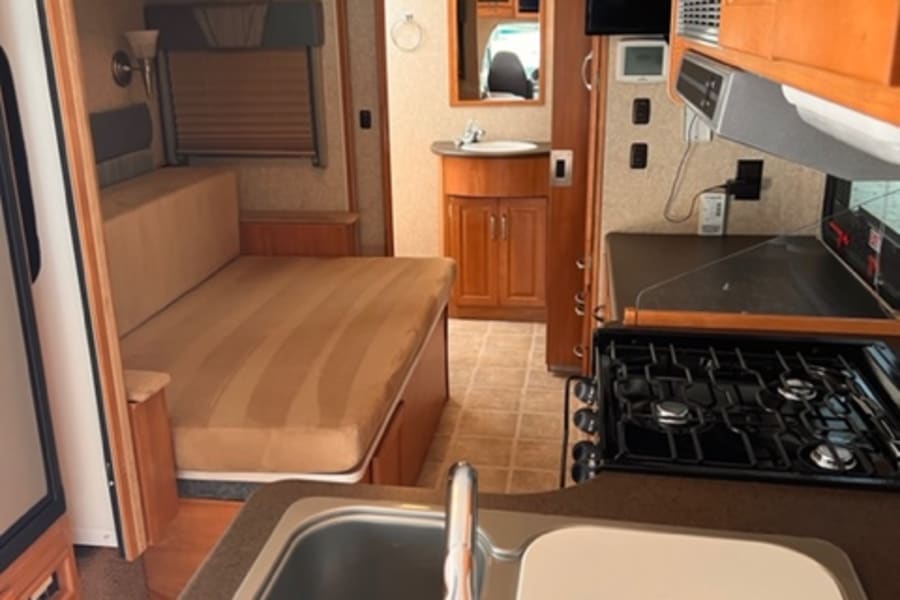 This RV rental offers a well-equipped kitchen (sink, stove, microwave), a living area with TV, and cozy sleeping space.