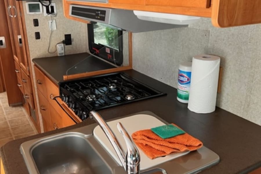 RV rental kitchen: Clean, functional space with microwave, gas stove, sink, and wood cabinets. Essential for travel cooking.