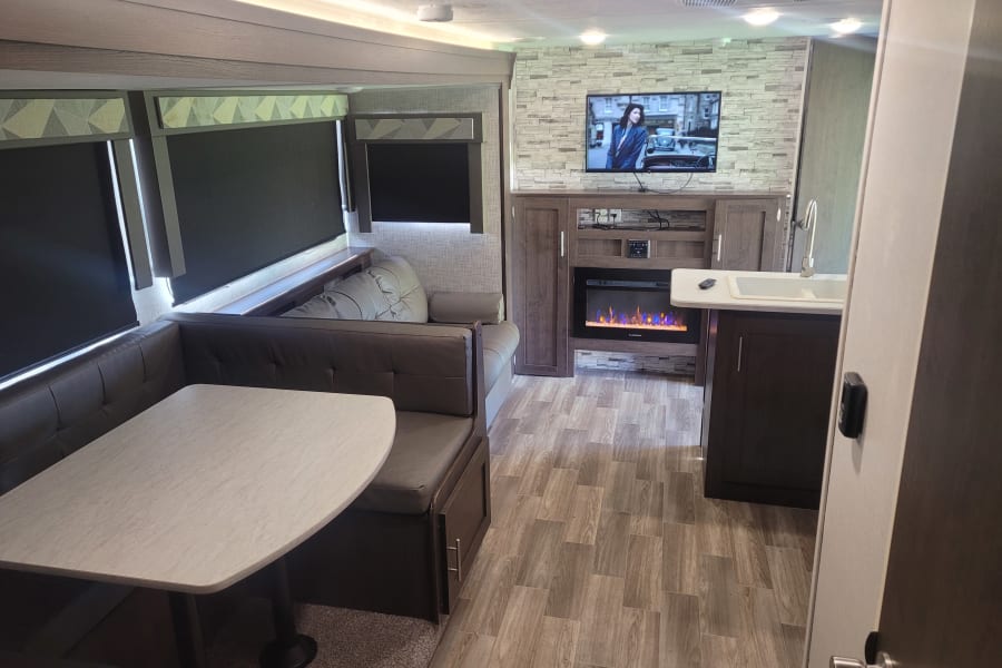 Inside this inviting RV rental: dinette, lounge, entertainment center with TV, fireplace, and functional kitchenette.