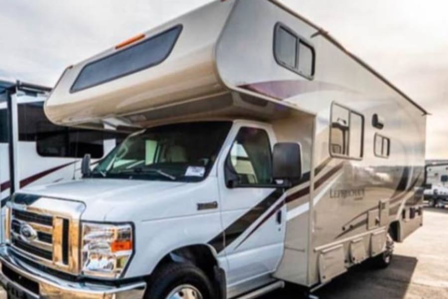 A white and beige Class C motorhome, a great choice for an rv rental, parked in an outdoor lot.