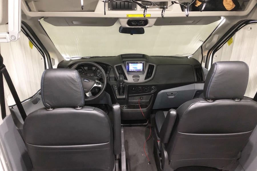 Spacious RV rental van interior, showing two dark front seats, the dashboard, and a sunshade on the windshield.