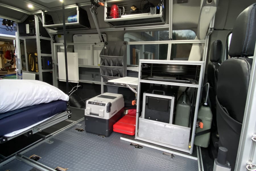 Modern rv rental interior: bed, Dometic cooler, ample modular storage, and diamond plate floor for adventure.