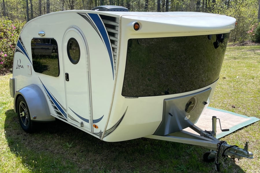 White & blue teardrop travel trailer for rv rental. Luna camper parked on grass, ready for adventure.