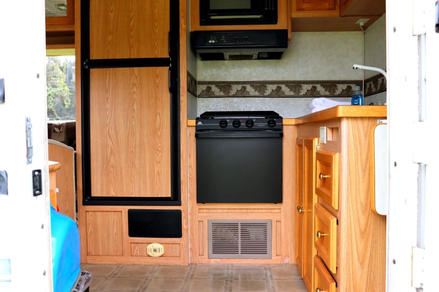 RV rental kitchen features: microwave, stove, fridge, sink, and cabinets. Ready for your adventure.