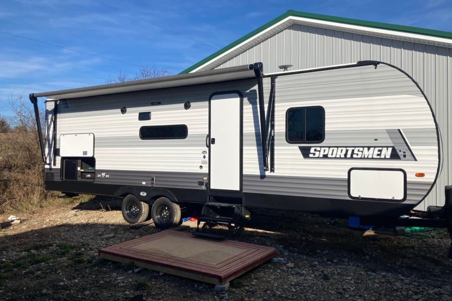 Modern RV rental travel trailer parked outdoors. Features an extended awning & entry platform for camping comfort.